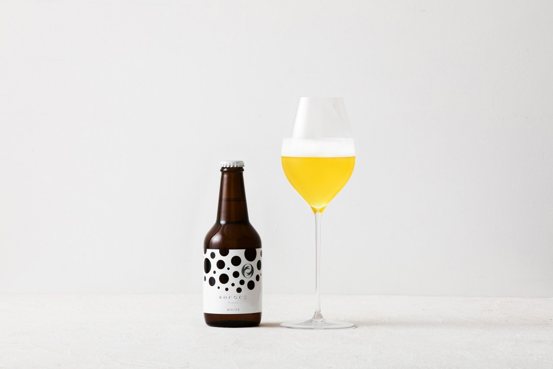 Maison Rococo luxury white beer bottle with goblet glass filled with pale yellow beer.