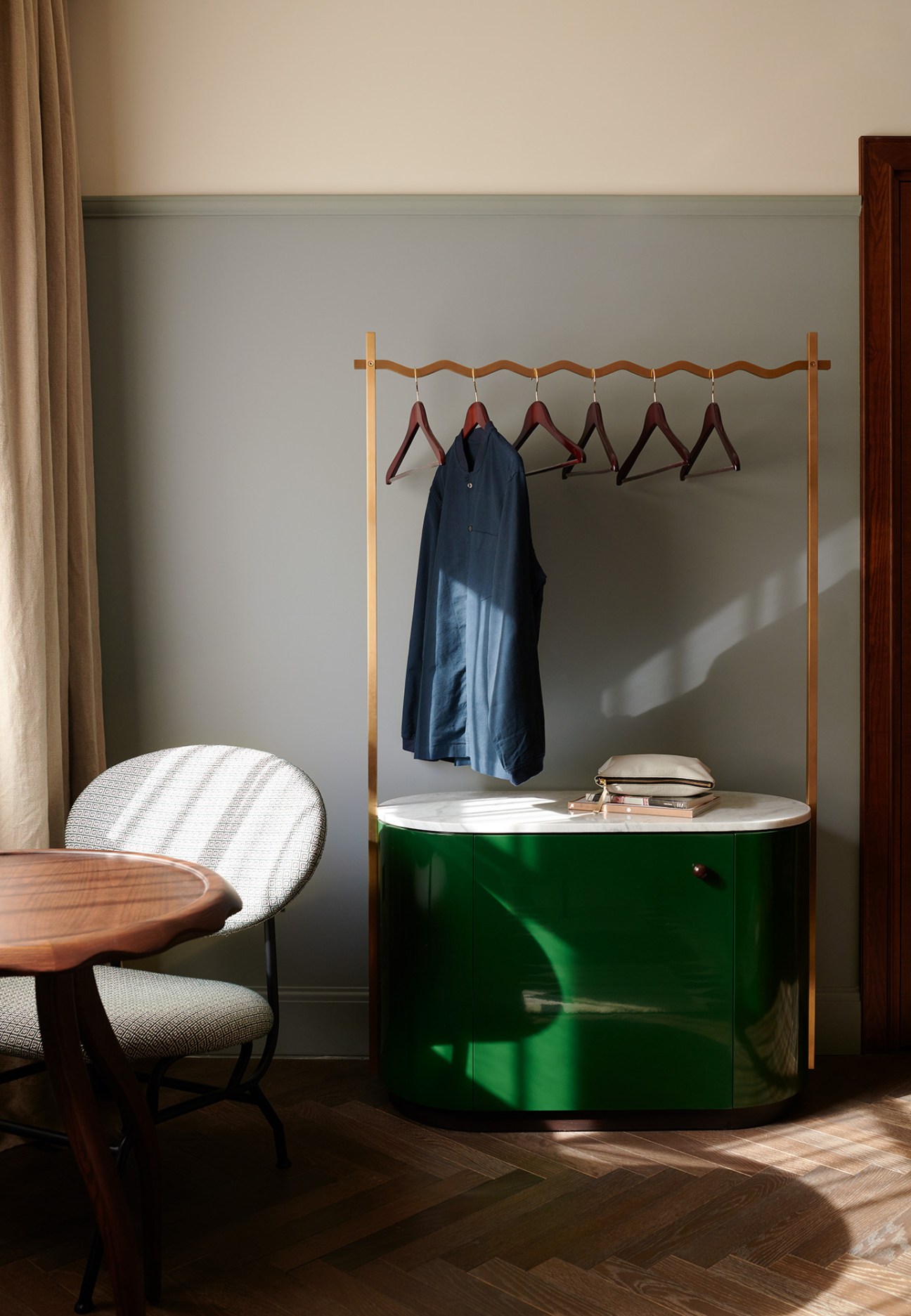 Modern hotel room interior with wooden clothing rack, green lacquered cabinet, and upholstered chair