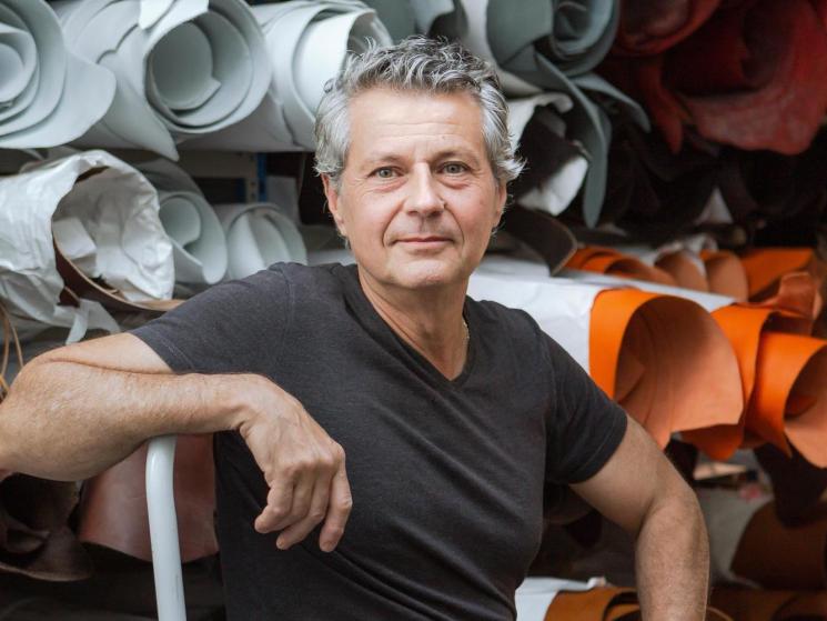 Alain Rondini sitting in his workshop surrounded by colorful leather materials and rolls