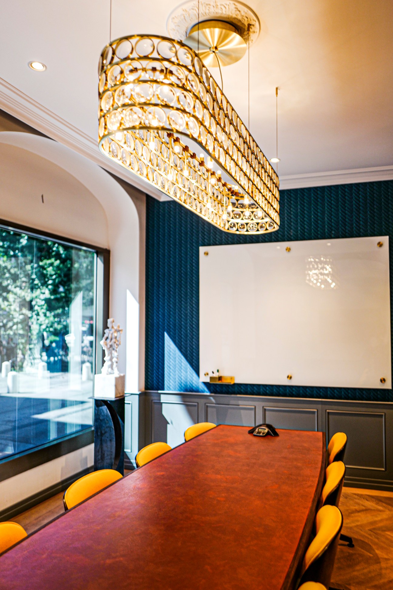 Conference room with ornate crystal chandelier, dark wood table, yellow chairs and navy accent wall