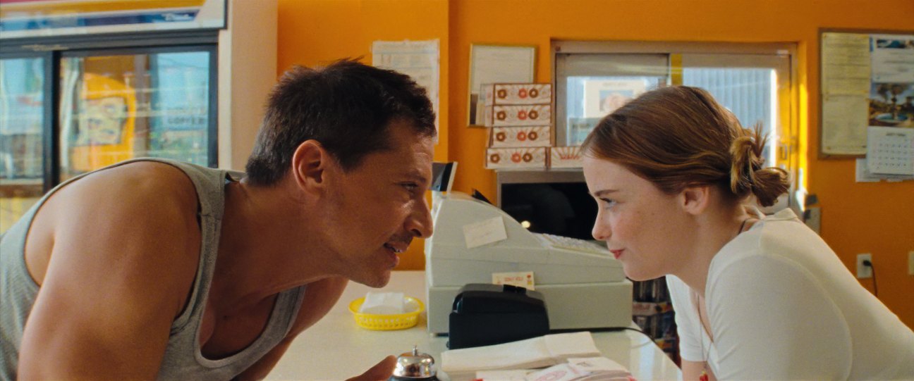 A man in a tank top and woman in white clothing lean toward each other looking at a microscope in a laboratory setting