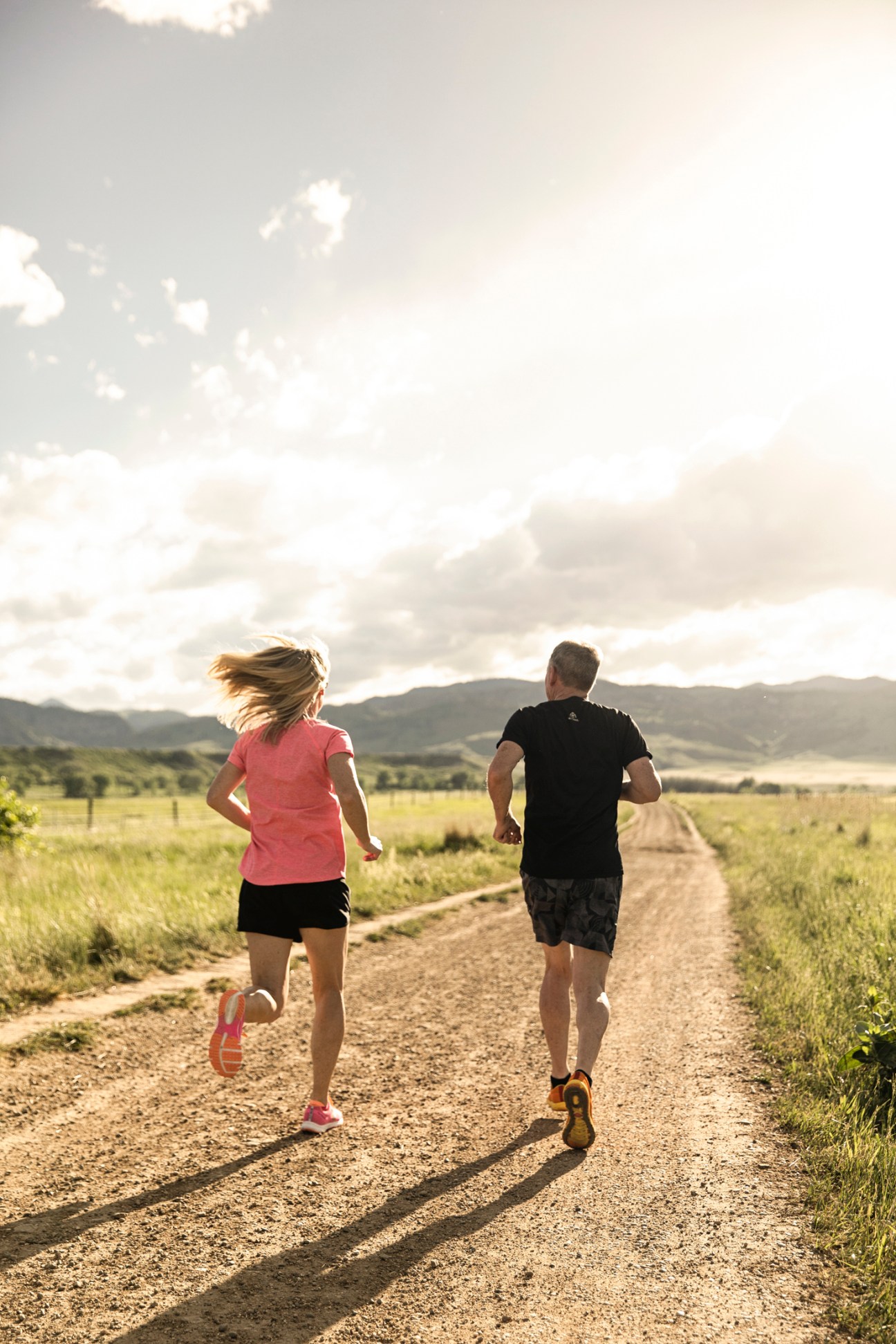 Two runners jogging on a dirt road through an open valley with mountains in the background.