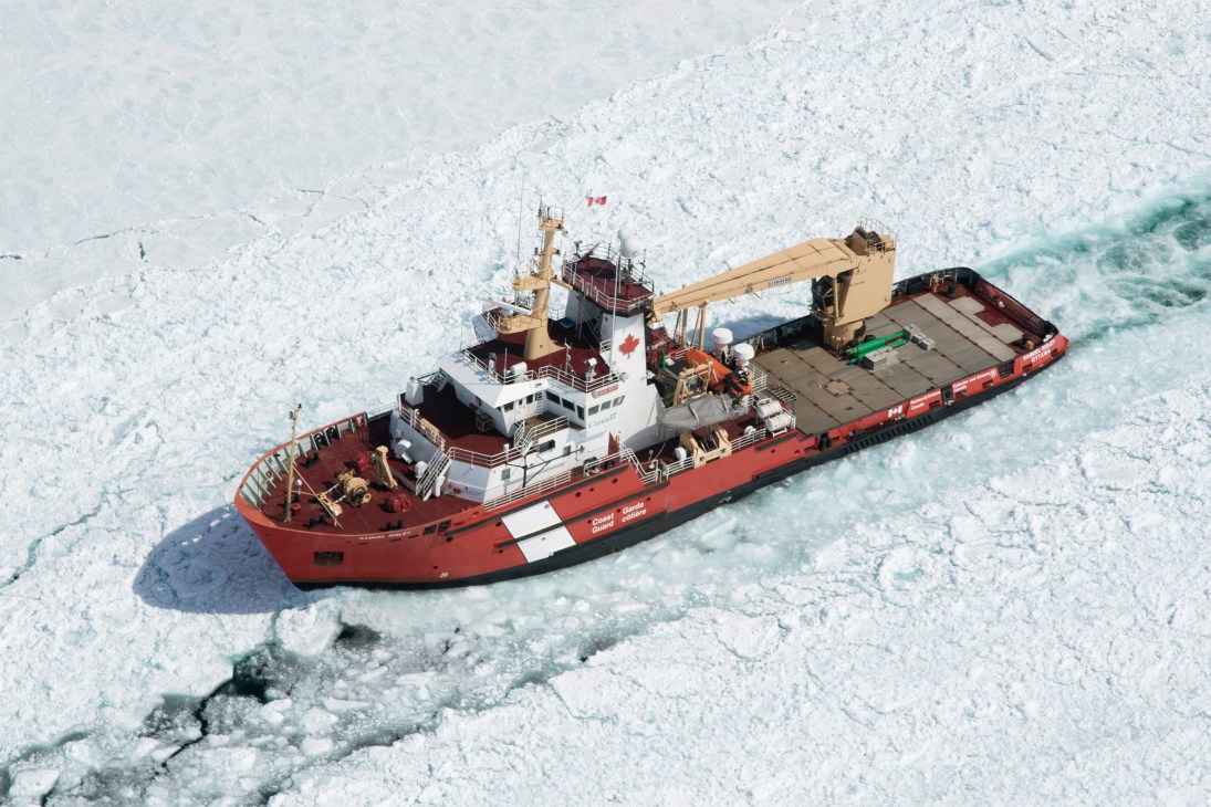 Red icebreaker ship with crane navigating through broken Arctic sea ice from aerial view