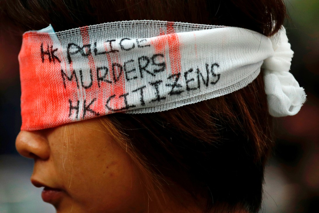 Protester wearing a white bandage across eyes with text reading 'HK POLICE MURDERS HK CITIZENS'
