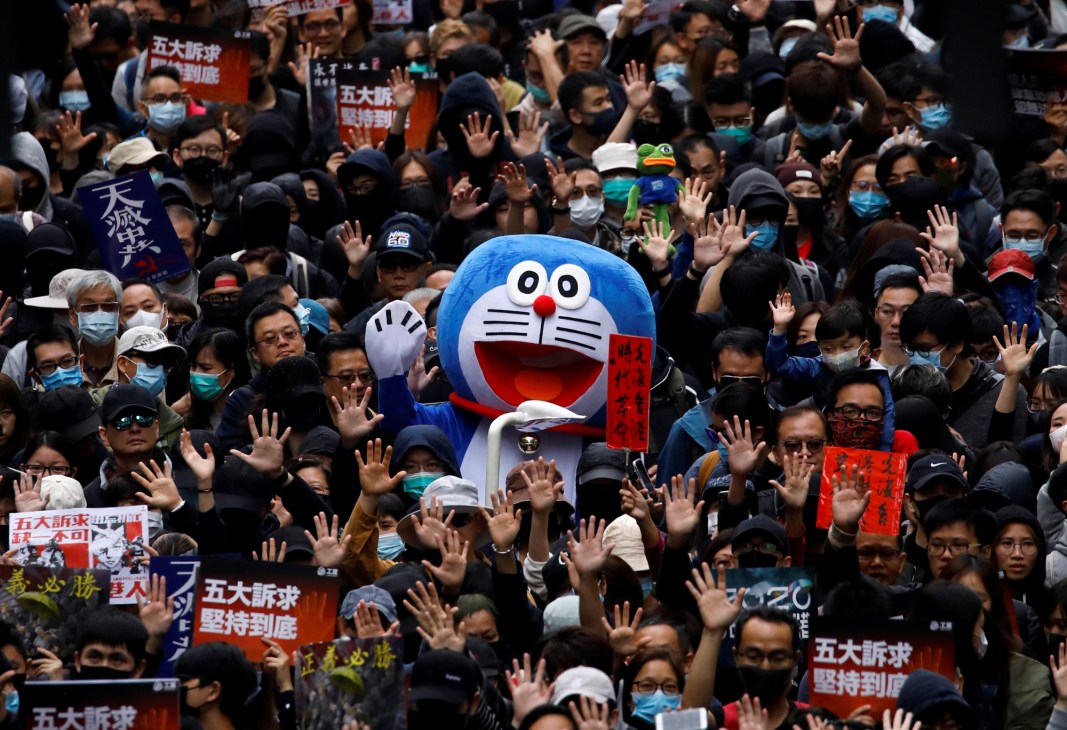 Hong Kong pro-democracy protesters with raised hands surrounding a large blue Doraemon character effigy amid crowd