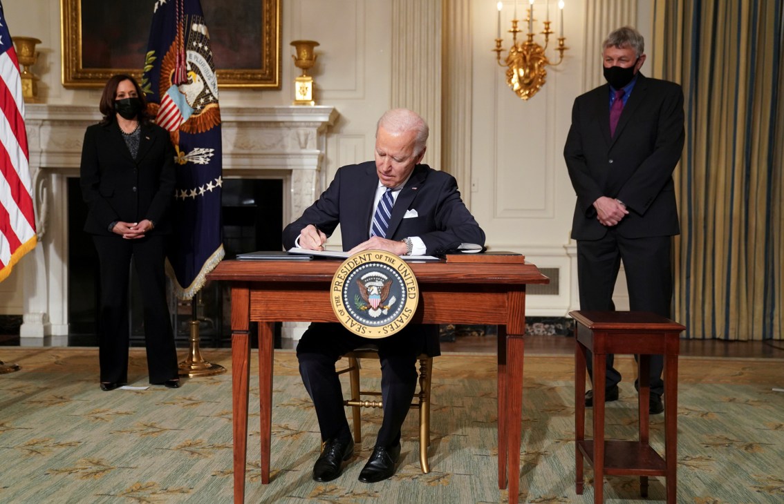 Biden signing an executive order at the Oval Office desk