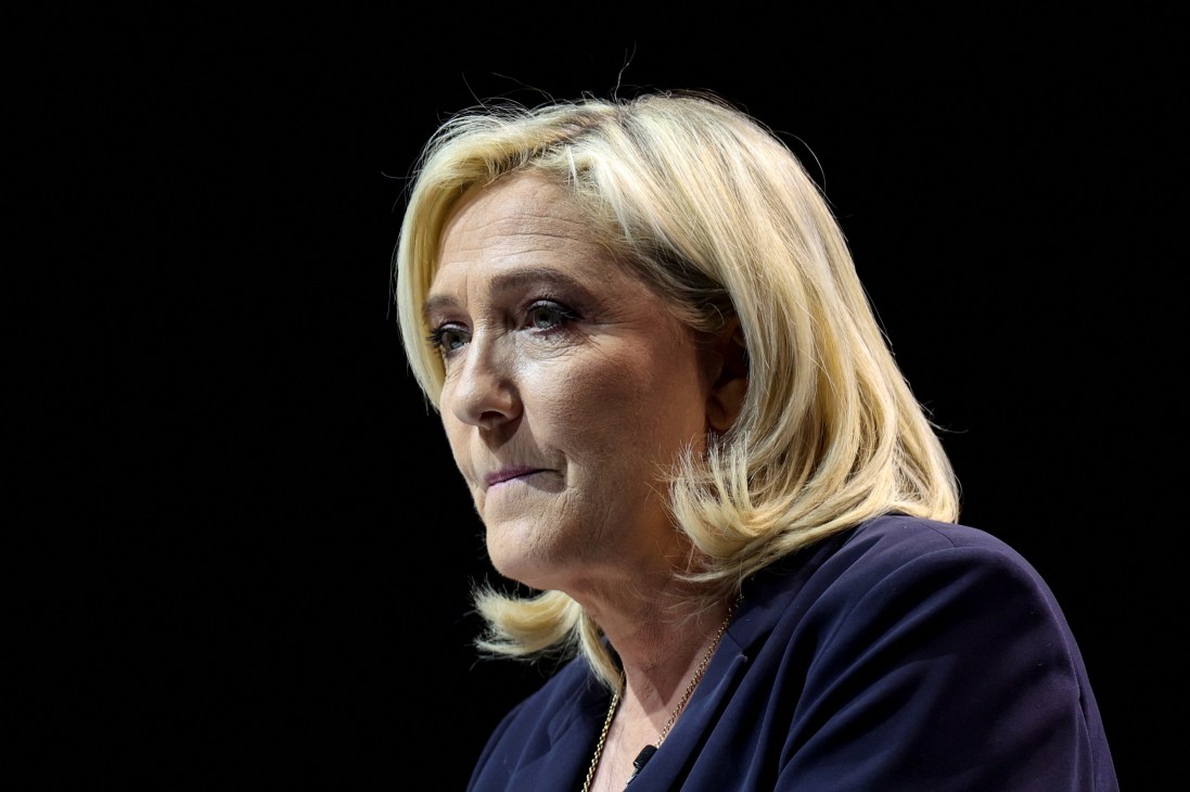 Woman with blonde hair in navy blue clothing looking to the side against dark background