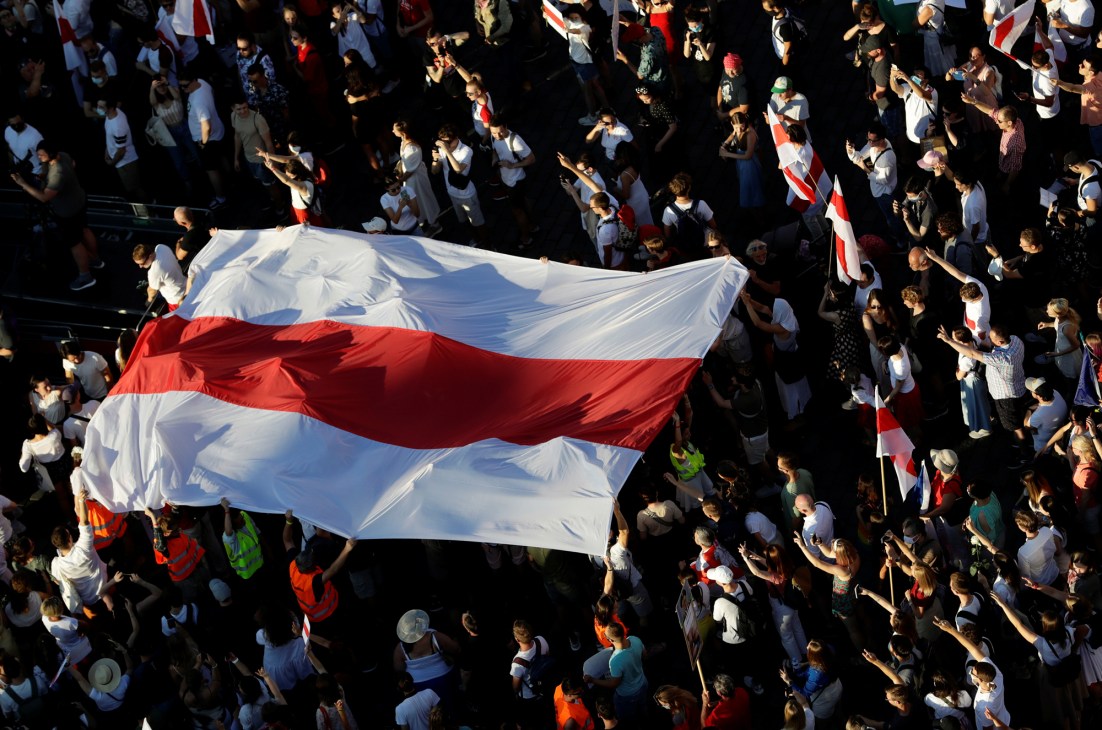Overhead view of protesters holding a large white-red-white historical flag of Belarus during a demonstration in Prague.