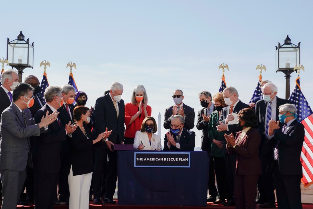 Nancy Pelosi signing the American Rescue Plan Act with multiple pens at a ceremony