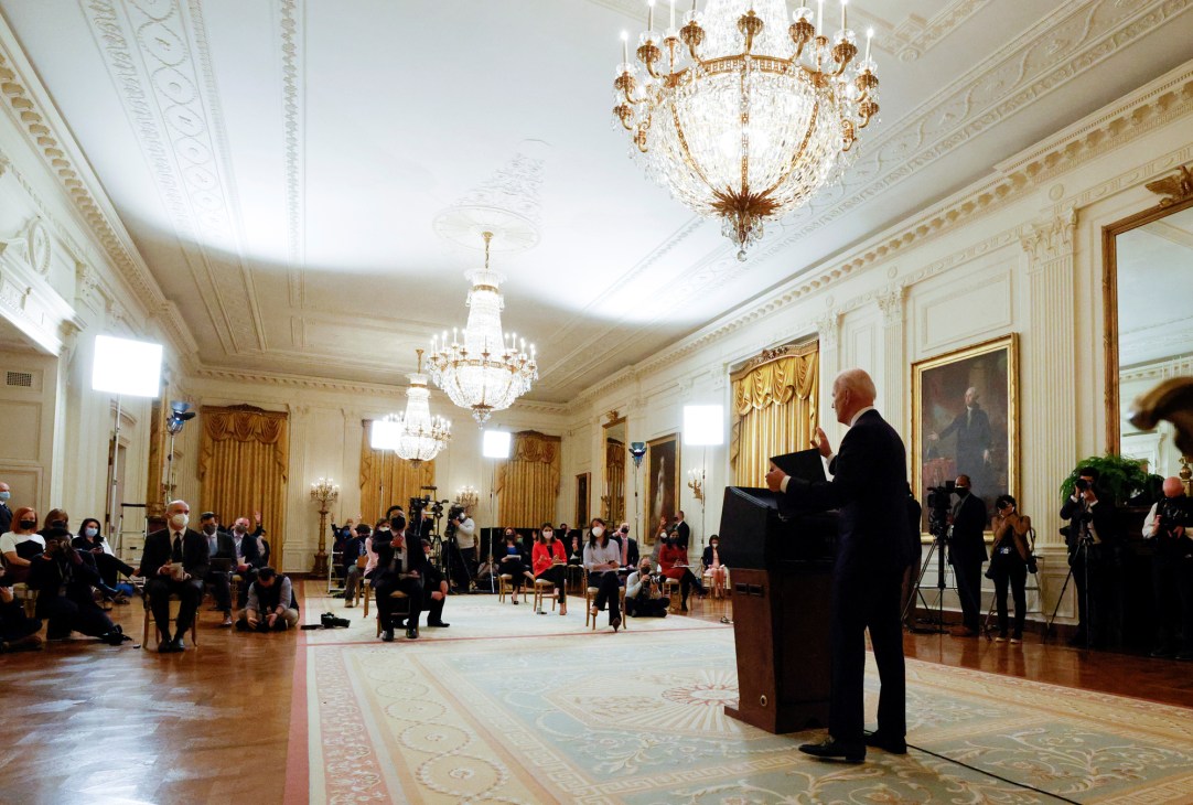 Biden standing behind a podium taking questions from reporters at a White House press conference