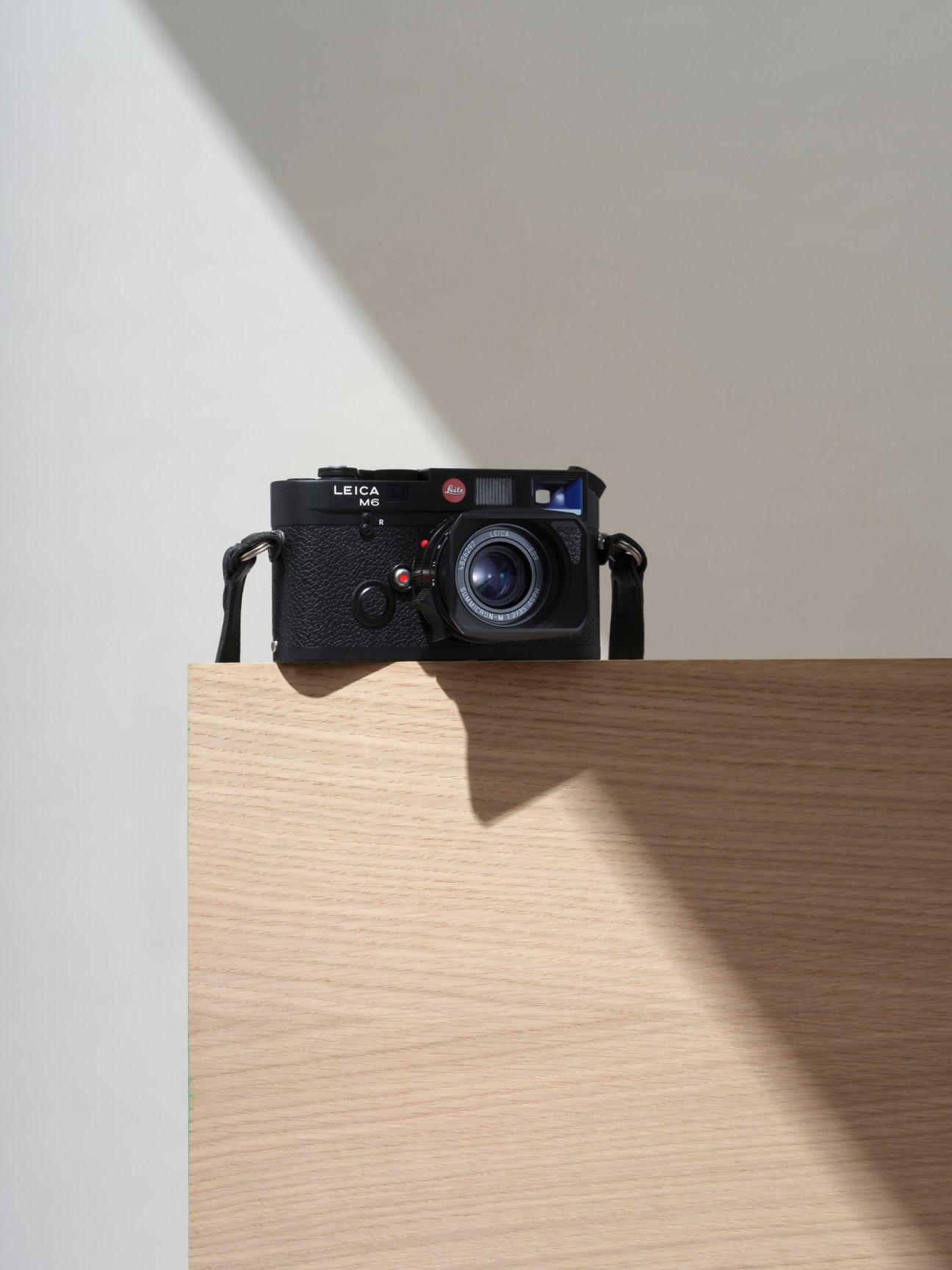 Black Leica M6 analog camera with strap positioned on light wooden surface against neutral background