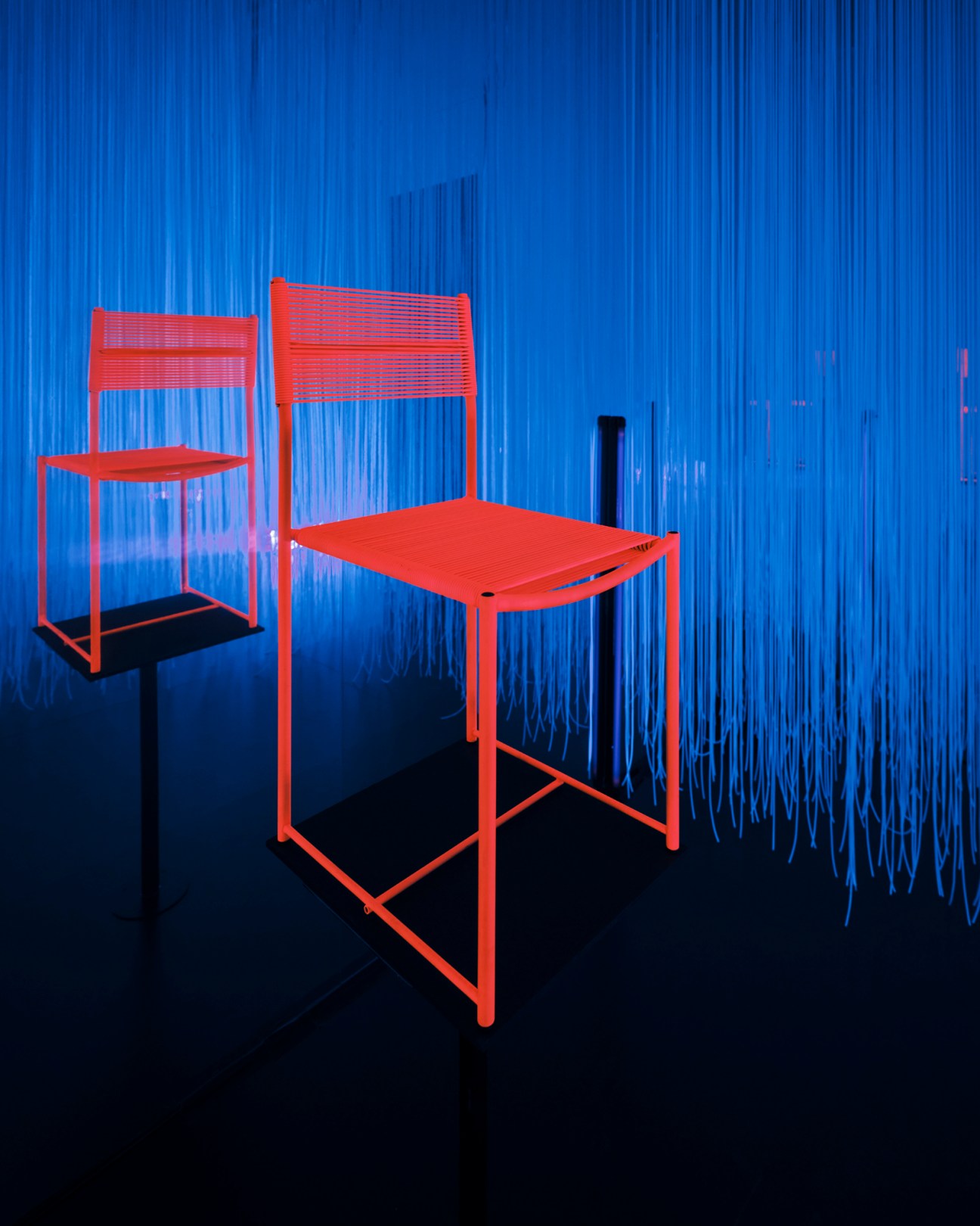 Spaghetti chair by Giandomenico Belotti for Alias with red metal frame and blue rope weaving displayed with dramatic lighting