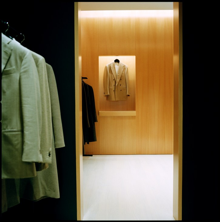 Minimalist retail showroom with wooden walls displaying a caramel-colored double-breasted blazer on a mannequin.