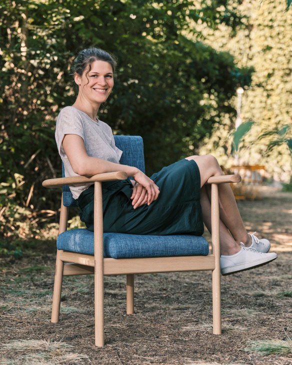 Sarah Hossli sits in the Lotte chair, an inclusive design featuring extended armrests that assist users in standing up.
