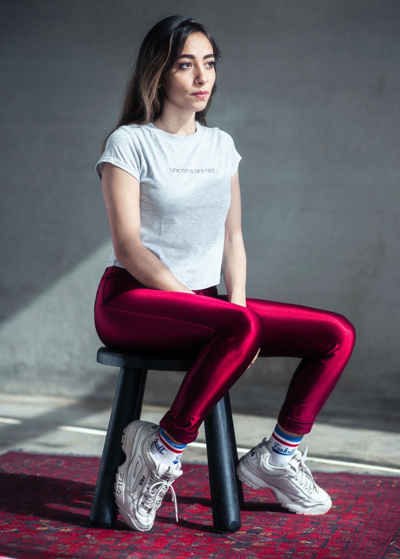 Sarah Taibah, Saudi actress and writer, sitting on a stool wearing a white t-shirt and red leggings