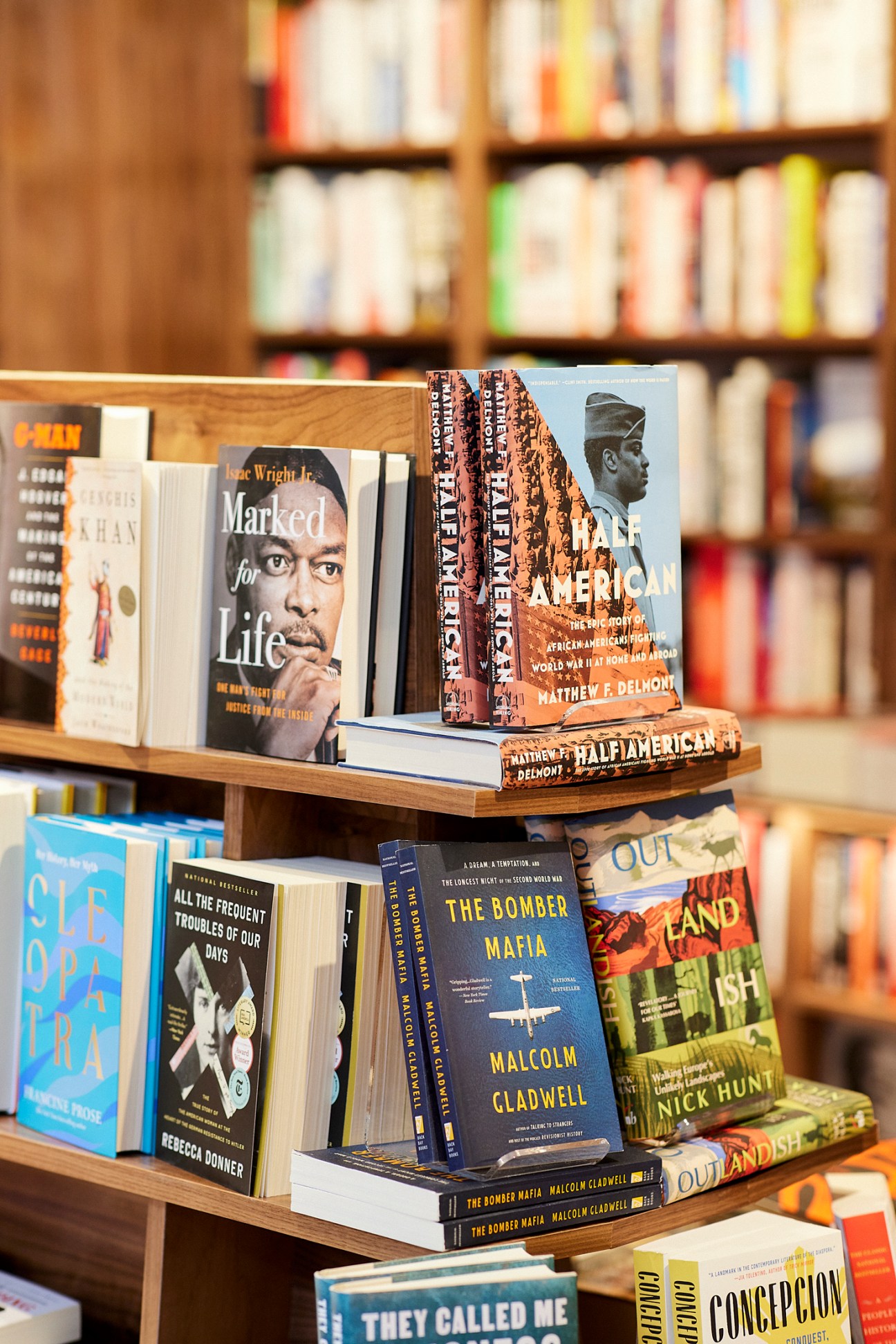 Wooden bookshelf display showing stacked books including titles by Malcolm Gladwell and other authors in bookstore