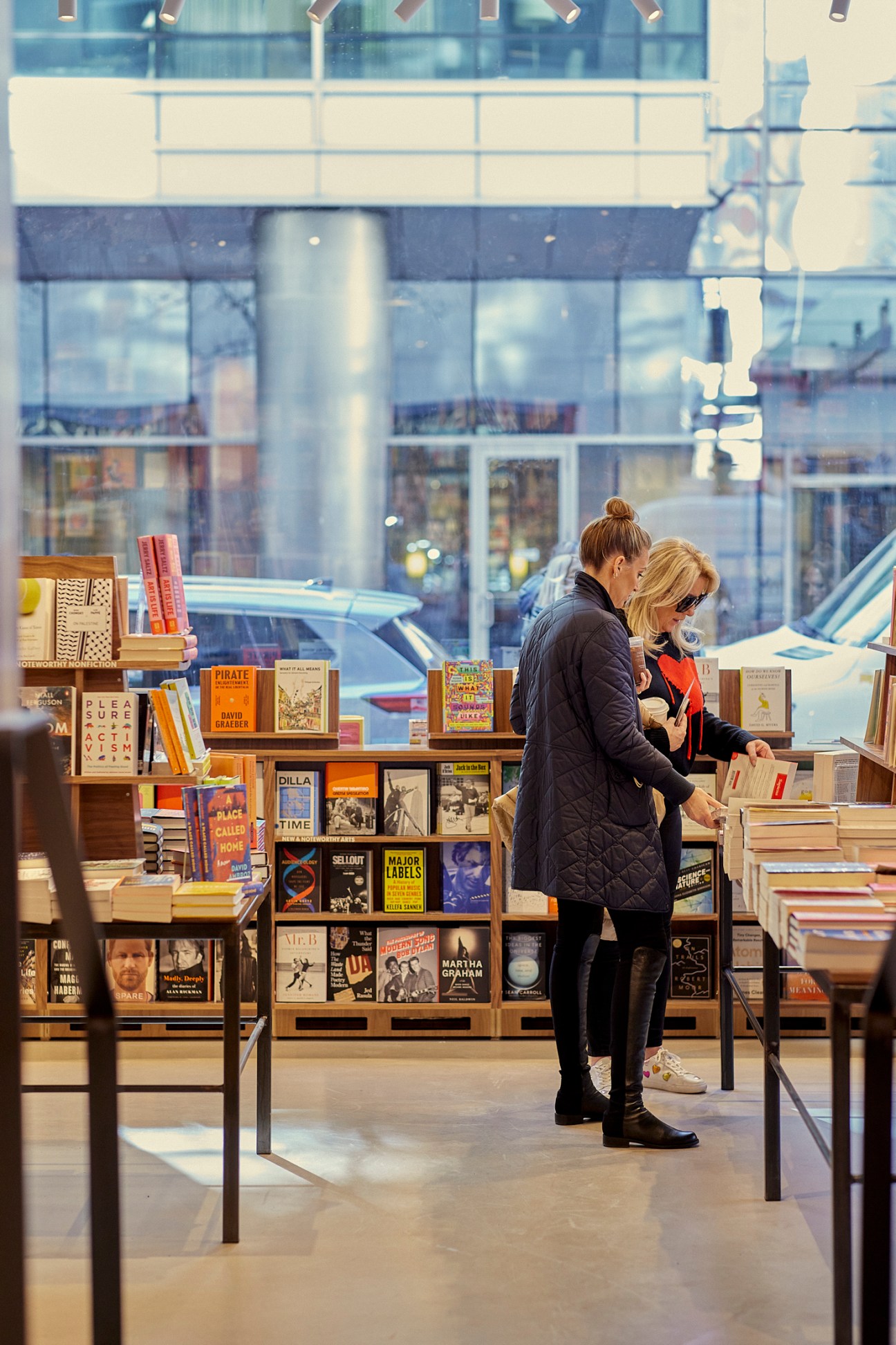 Two women browsing books on wooden shelves in McNally Jackson bookstore