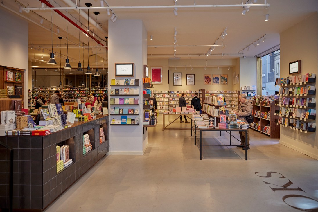 Interior view of McNally Jackson bookstore showing customers browsing wooden bookshelves and modern lighting