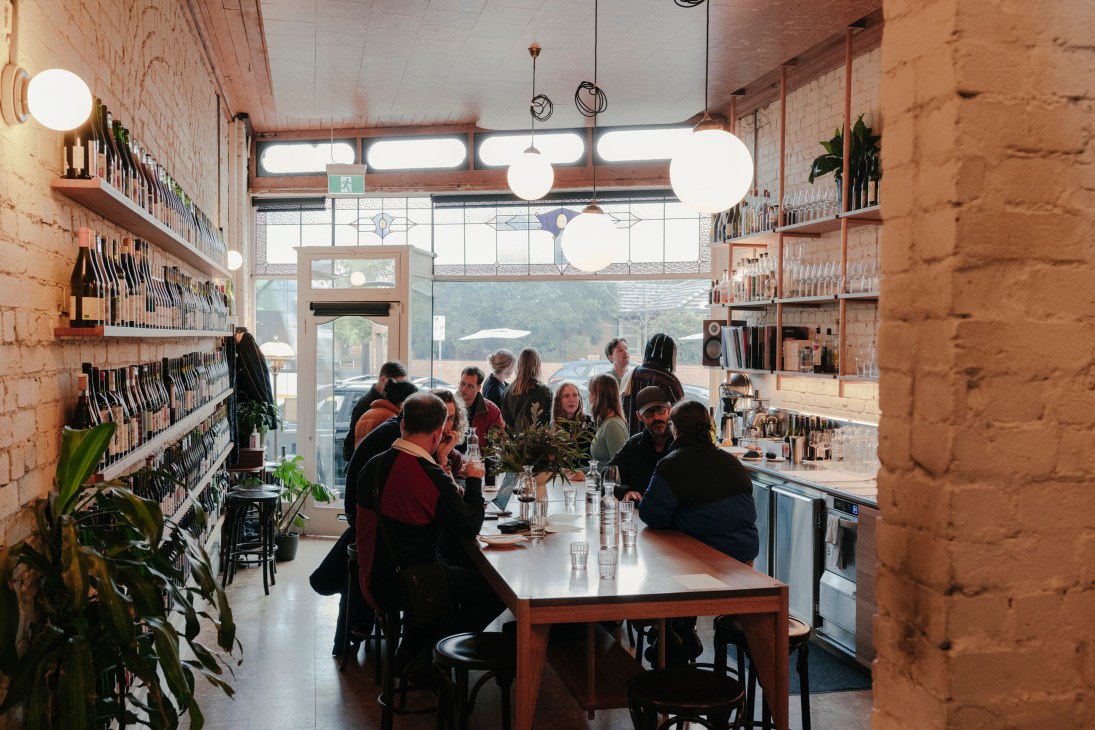 Interior view of Public Wine Shop in Melbourne showing exposed brick walls, wooden shelving with wine bottles, and diners