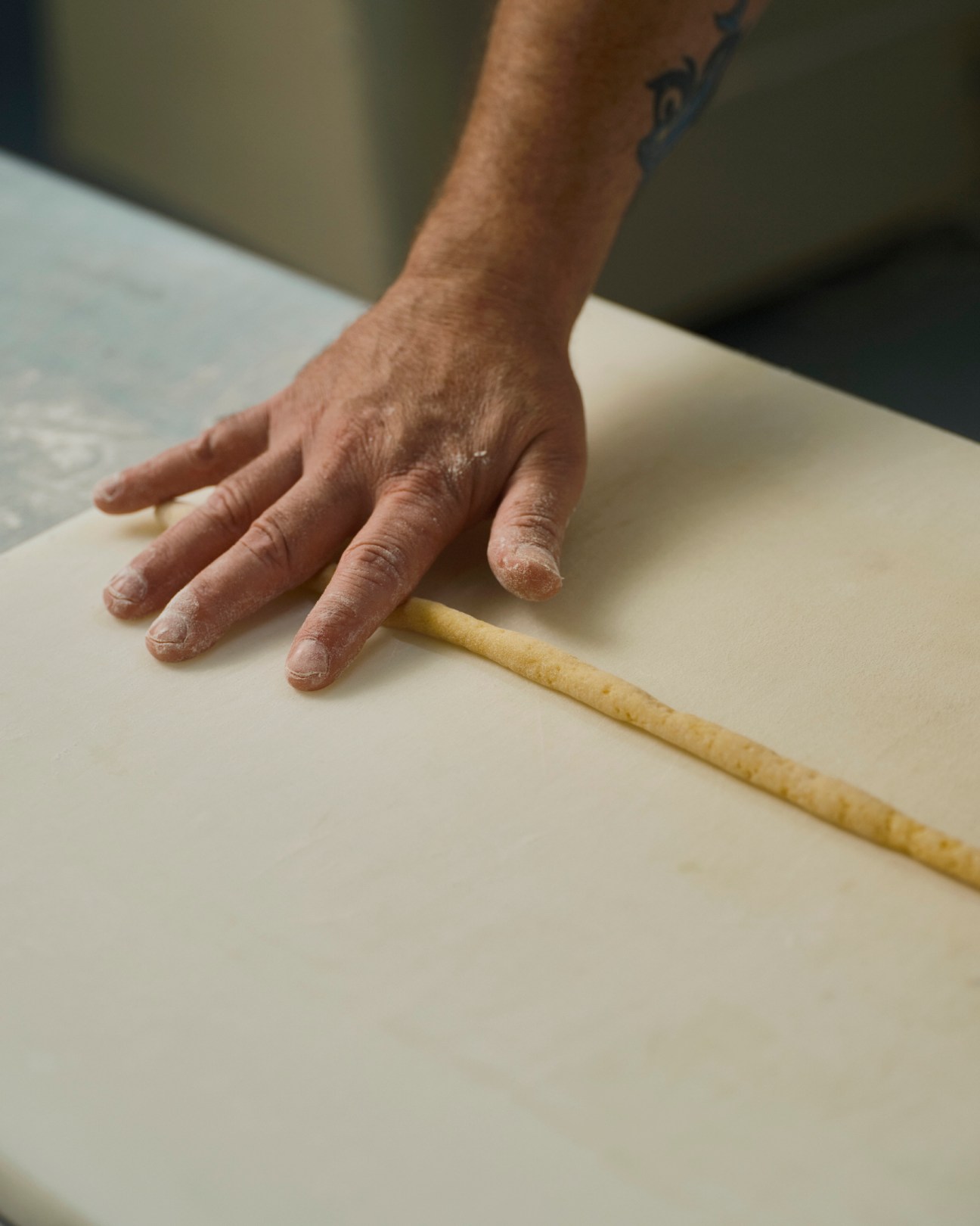 Hand rolling pastry dough with a wooden pin on a white surface during Scaturchio pastry preparation.