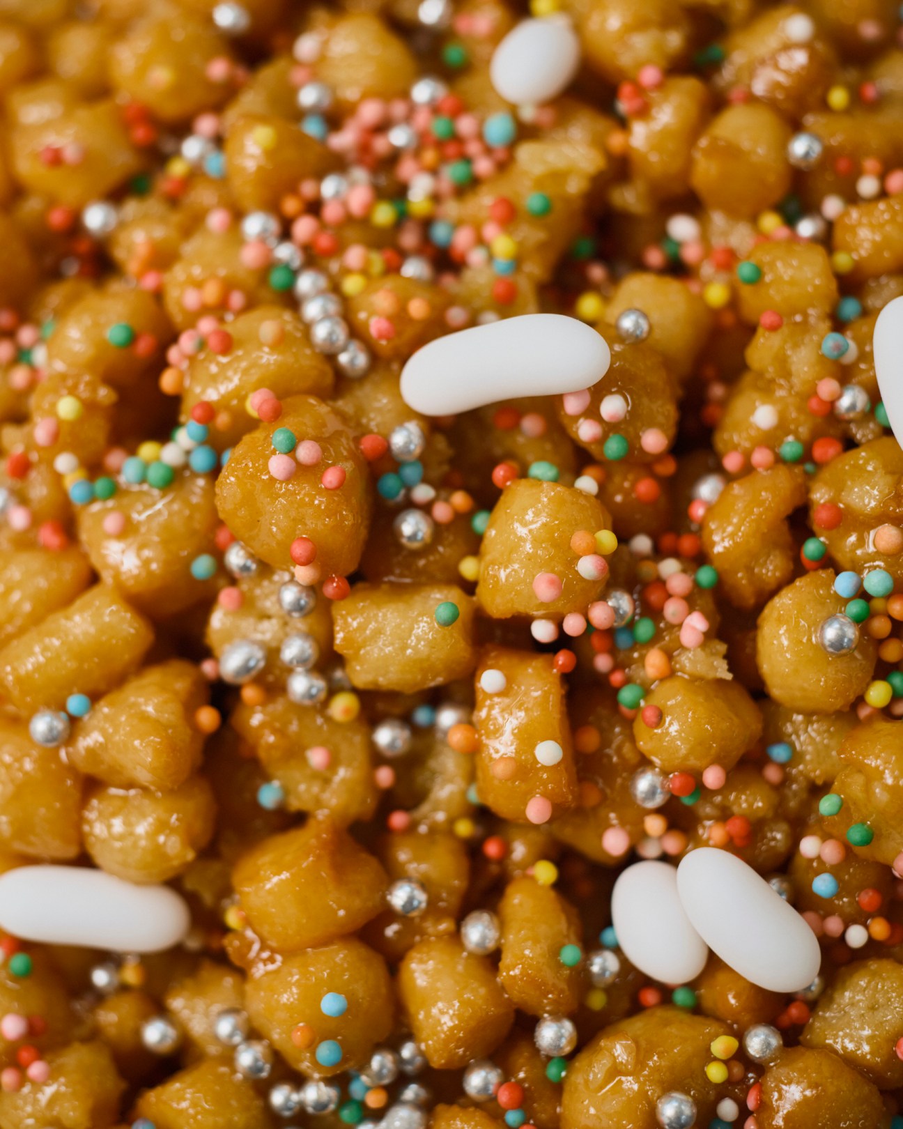 Golden fried dough balls topped with colorful sprinkles and white almond decorations.