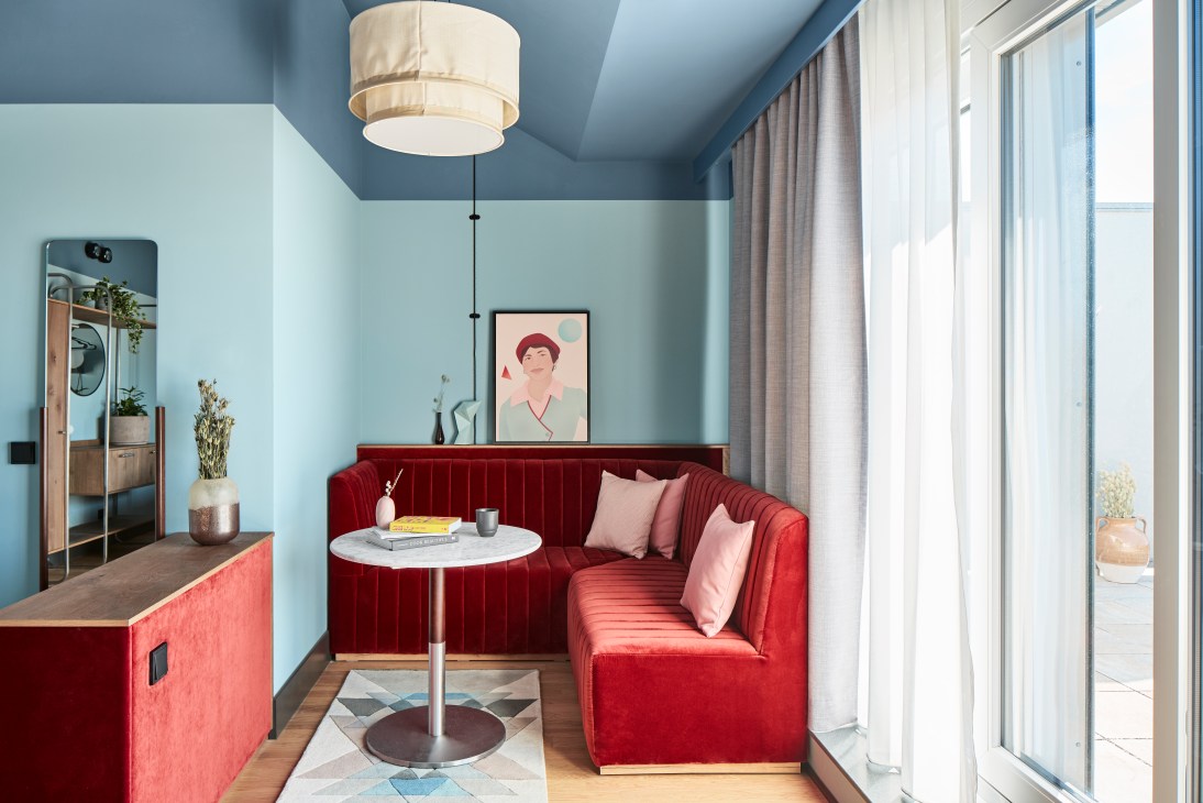 Modern hotel communal area with red velvet seating, blue walls, and contemporary furnishings.