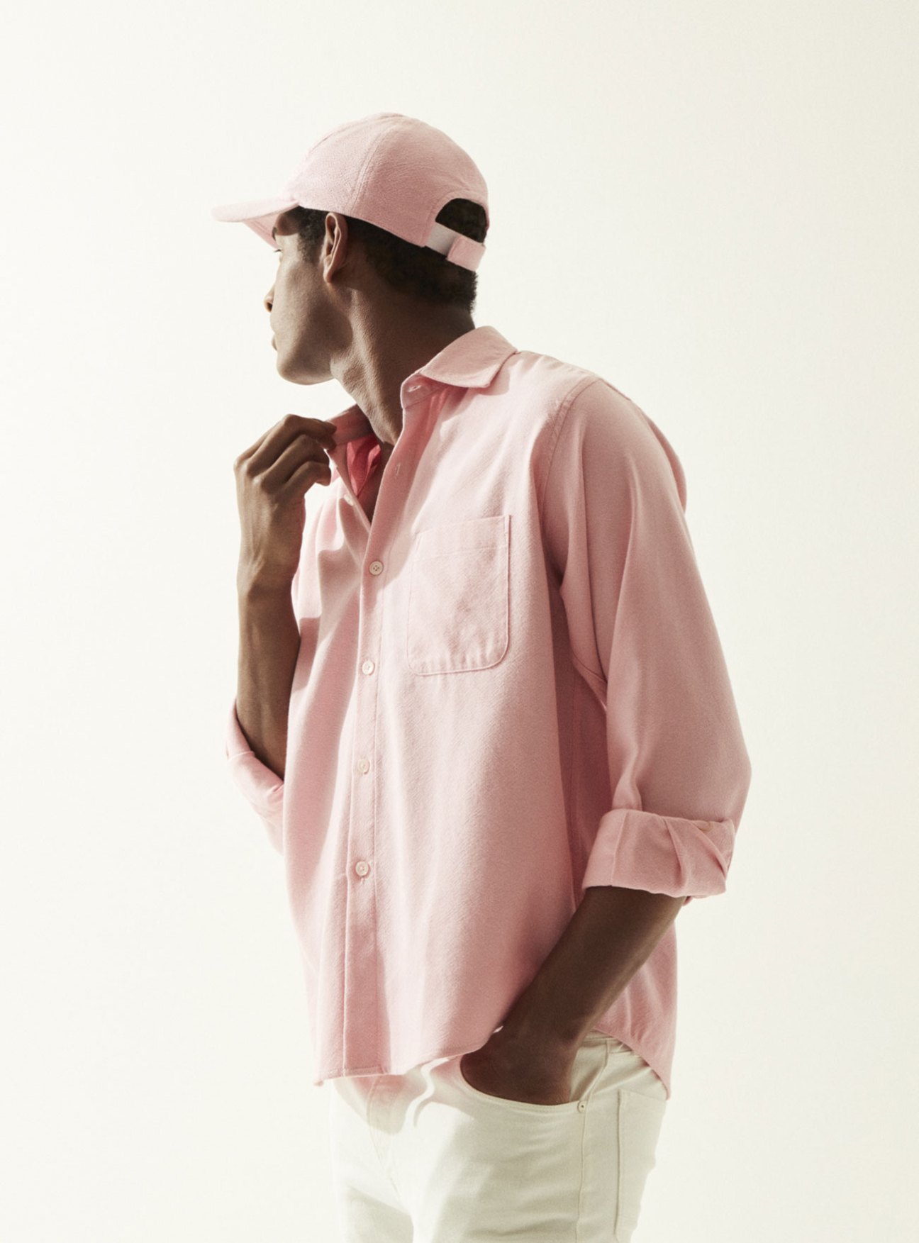 Man wearing pink shirt and cap by Marrakshi Life with cream jeans, shown in profile against neutral background.