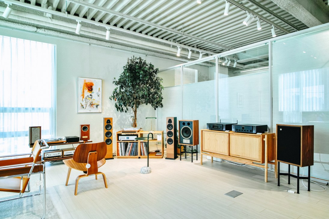 Mid-century modern furniture and audio equipment displayed in a bright, minimalist retail space with industrial ceiling.