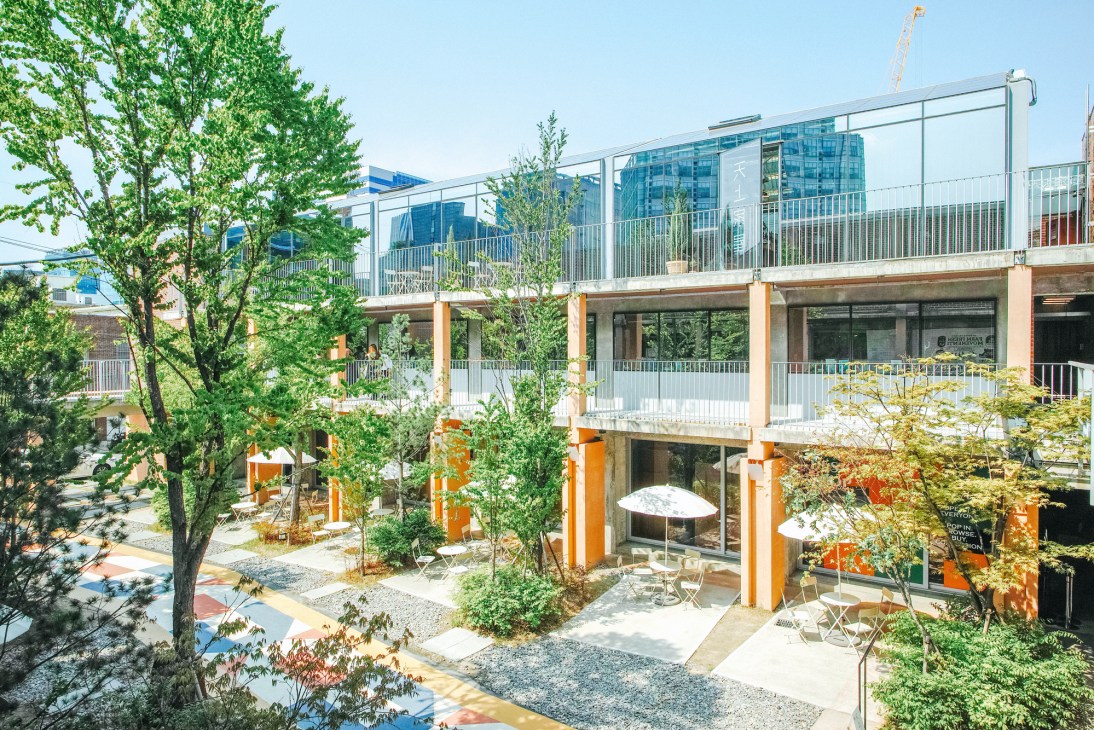 Modern converted factory building in Seongsu with orange pillars, glass railings, and green landscaping.