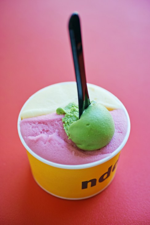 Pink and green gelato scoops in yellow NDD branded cup with black spoon on pink background