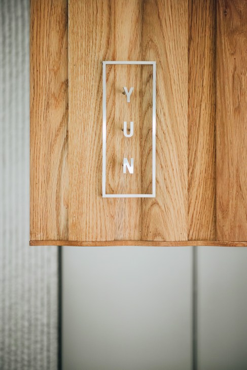 White rectangular logo with letters Y, U, N vertically arranged on natural wooden surface