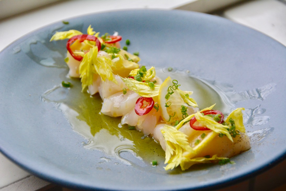 Sea scallop crudo with Meyer lemon, caper and couscous garnished with yellow and red chili on a blue plate.