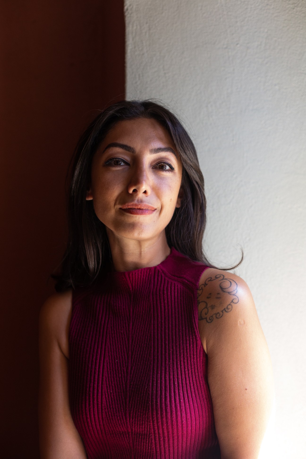 Portrait of film-maker Kivilcim Akay wearing a burgundy ribbed top with a tattoo visible on her shoulder