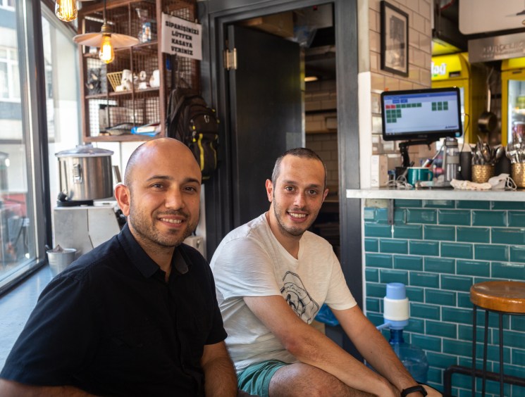 Two men sitting together in a modern restaurant with teal subway tile walls and industrial lighting