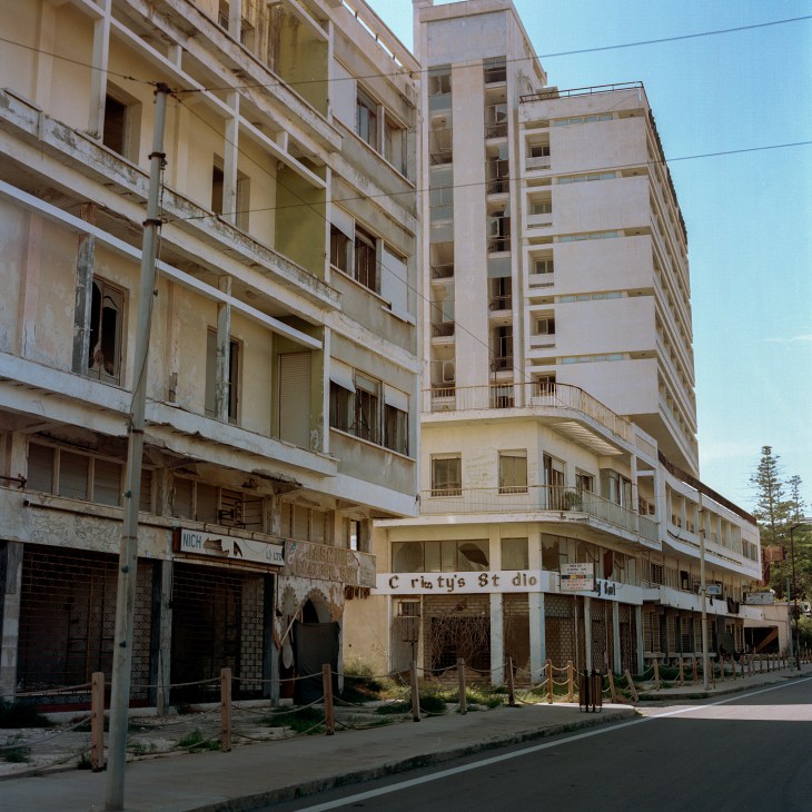 Abandoned multi-story buildings with balconies and shuttered storefronts on an empty street in Varosha