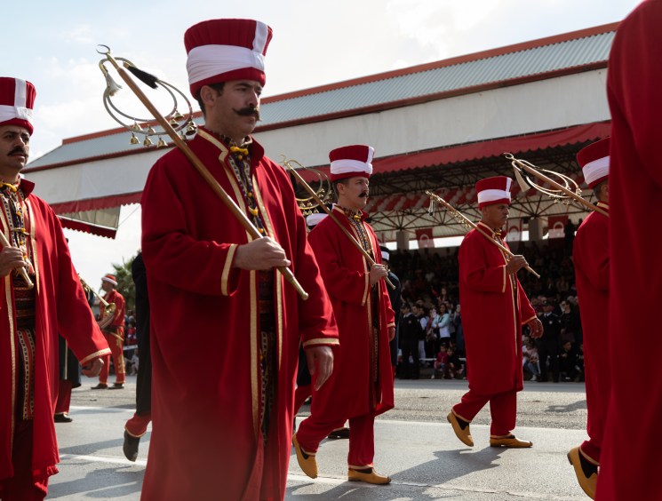 Turkish military band members in red uniforms and striped hats marching with ceremonial staffs at TRNC celebration