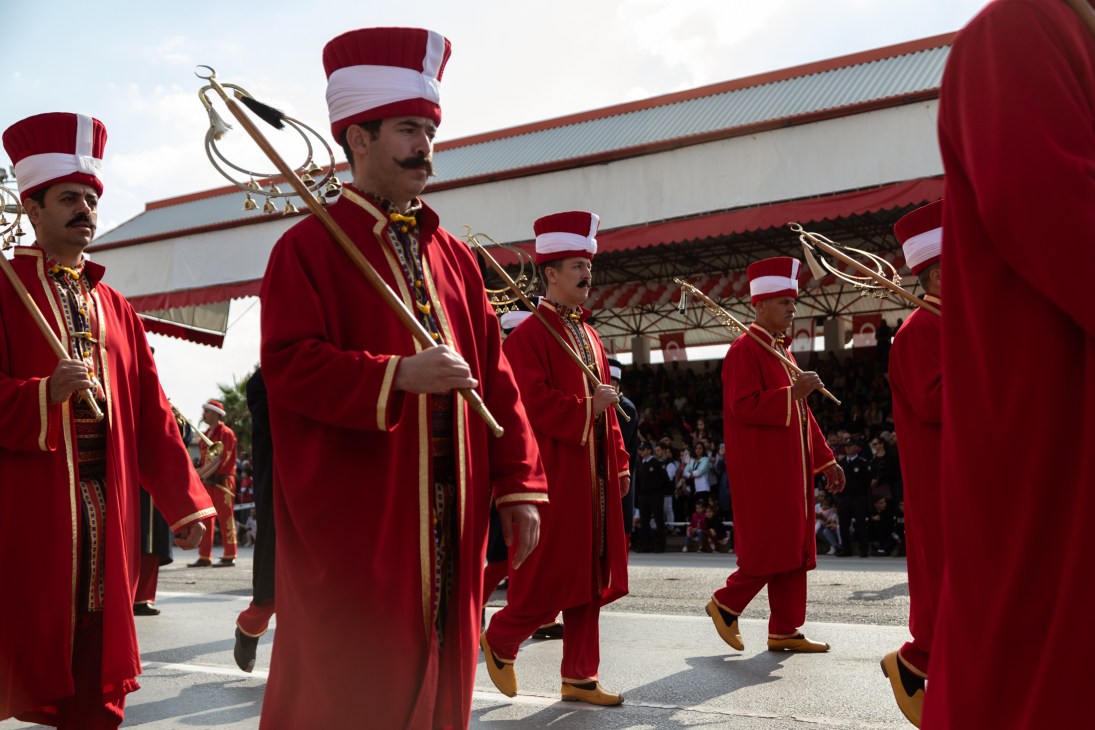 Turkish military band members in red uniforms and striped hats marching with ceremonial staffs at TRNC celebration