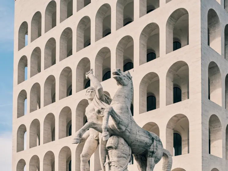 White modernist building with repetitive arched windows and classical statue in foreground