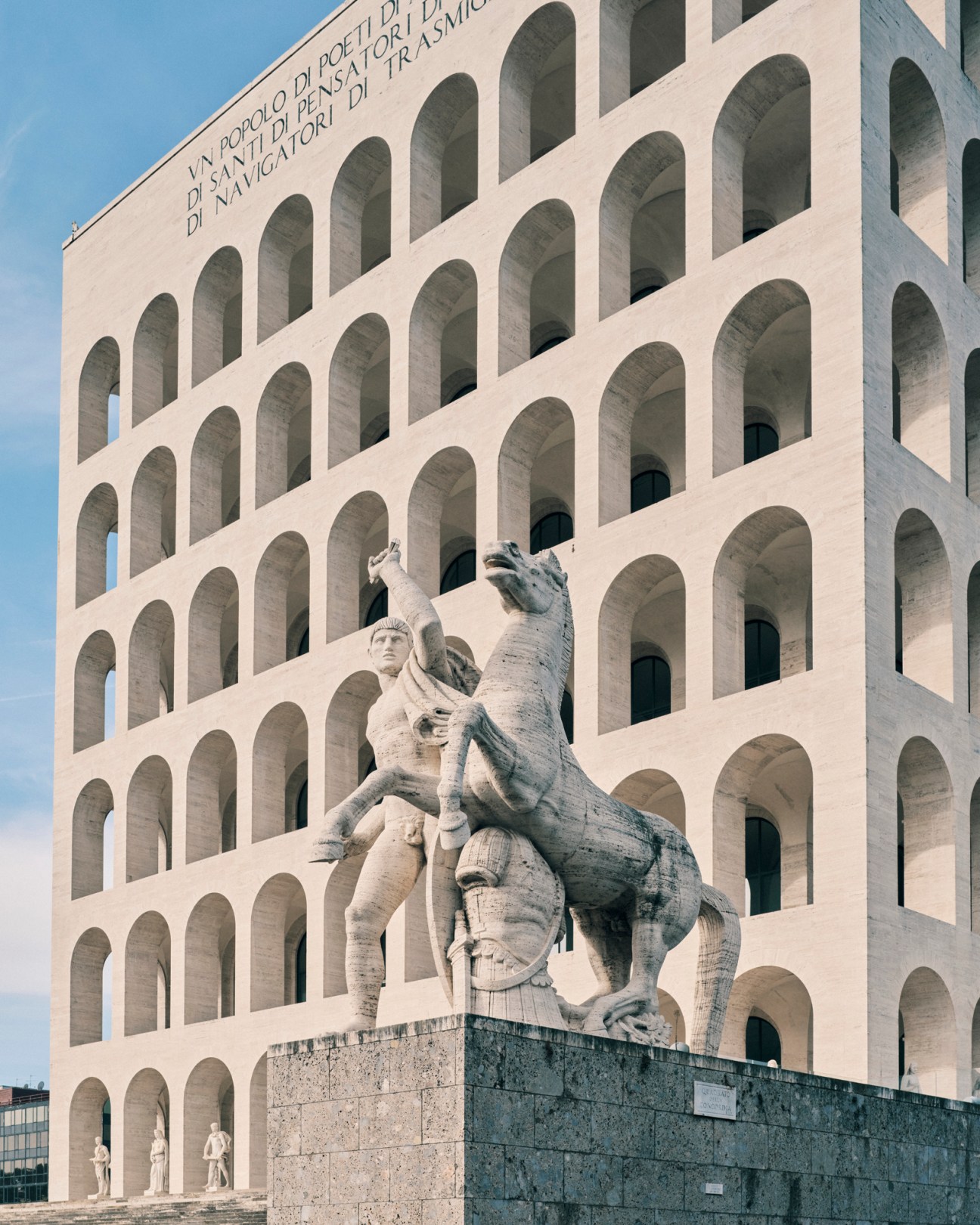 White modernist building with repetitive arched windows and classical statue in foreground