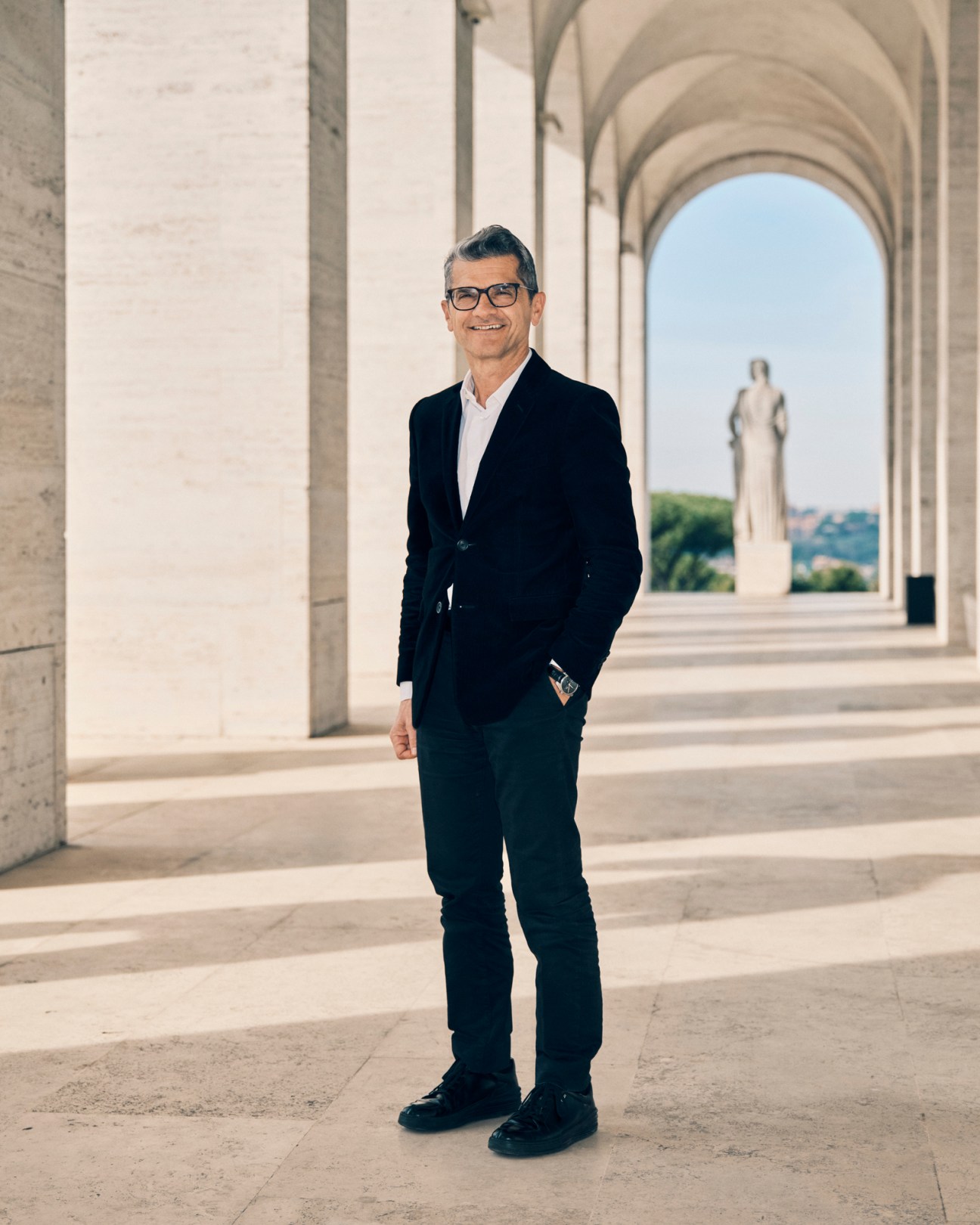 Serge Brunschwig standing in a columned archway wearing a dark suit and glasses