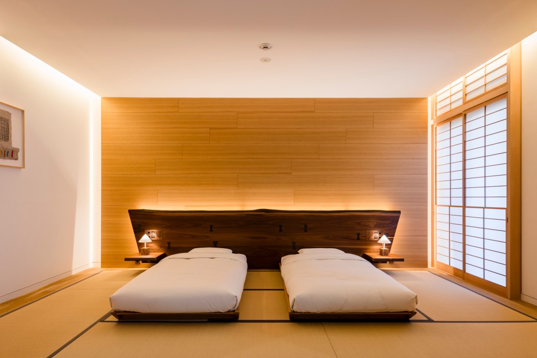 Japanese hotel bedroom with two low platform beds, wooden headboard, tatami mat flooring, and shoji screens