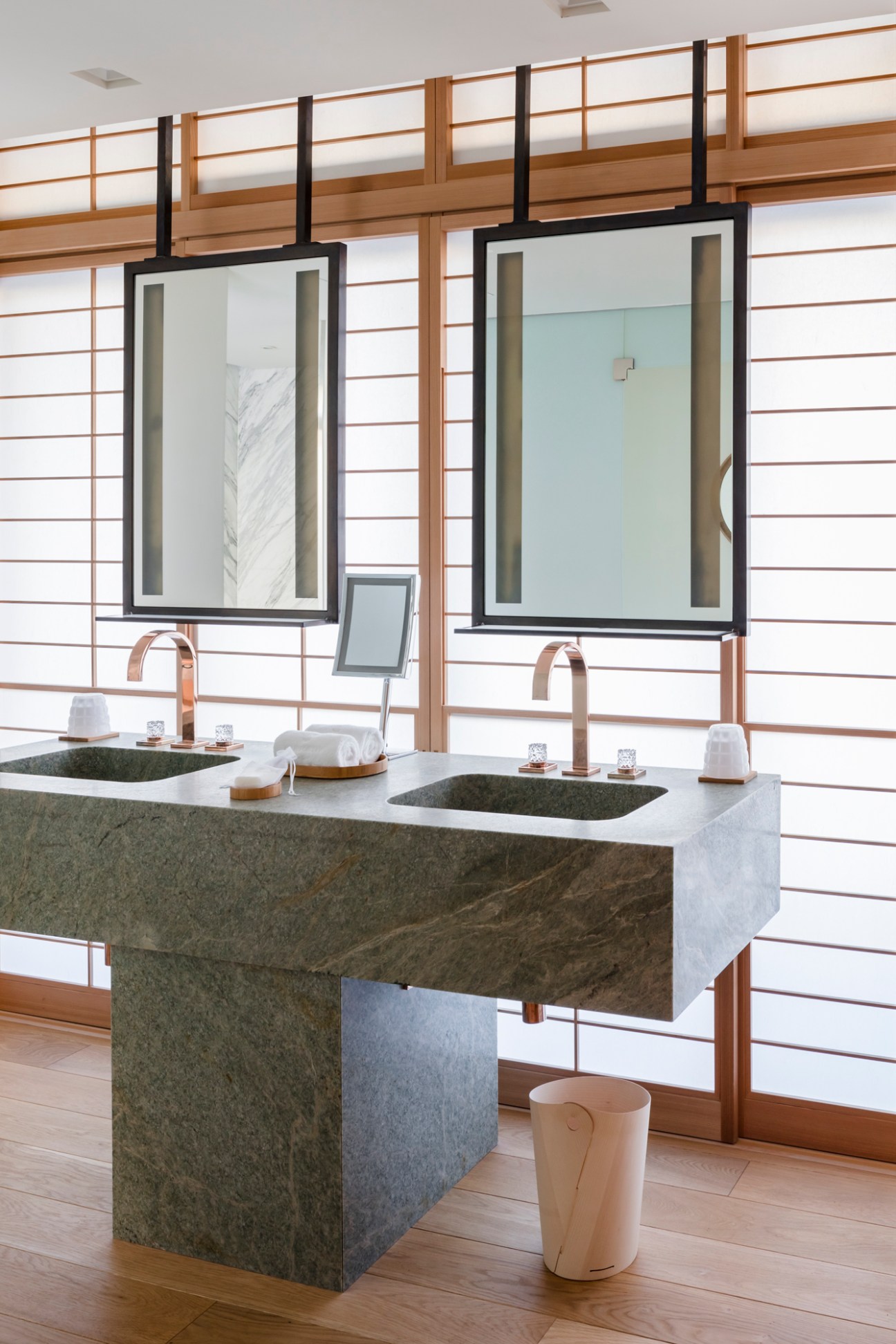 Modern bathroom vanity with marble double sink, copper faucets, and hanging mirrors with black frames
