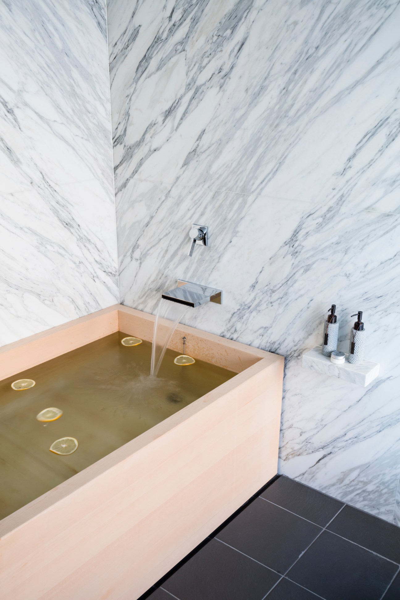 Hinoki wooden bathtub with marble walls and modern chrome faucet in luxury hotel bathroom