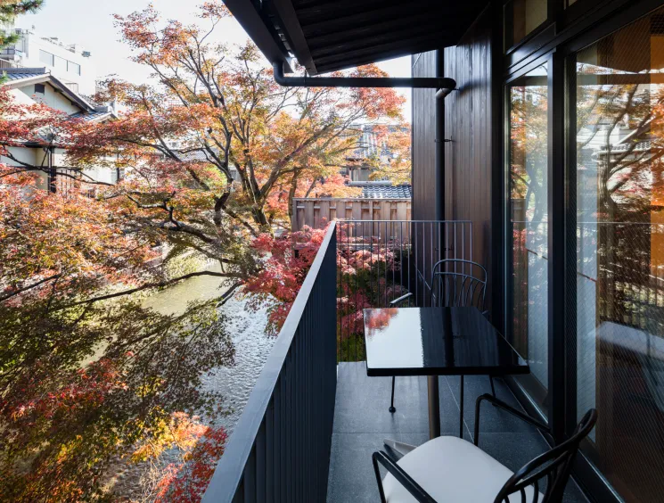Modern hotel balcony with black table and chairs overlooking autumn trees and river in Kyoto