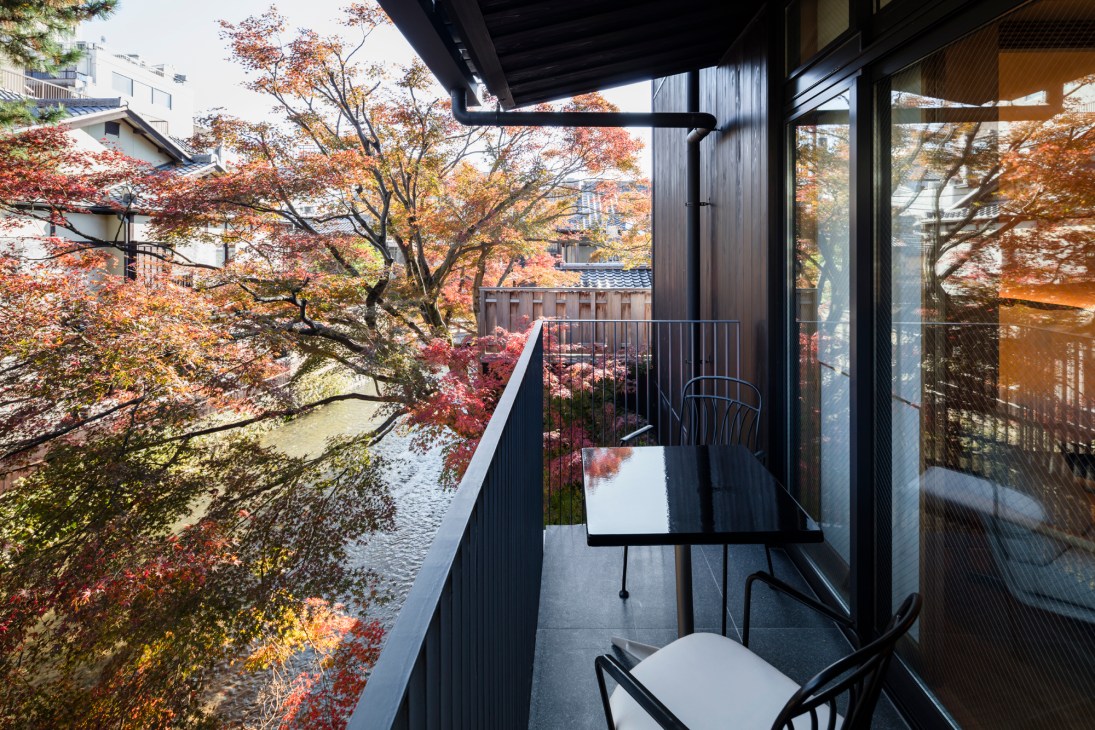 Modern hotel balcony with black table and chairs overlooking autumn trees and river in Kyoto