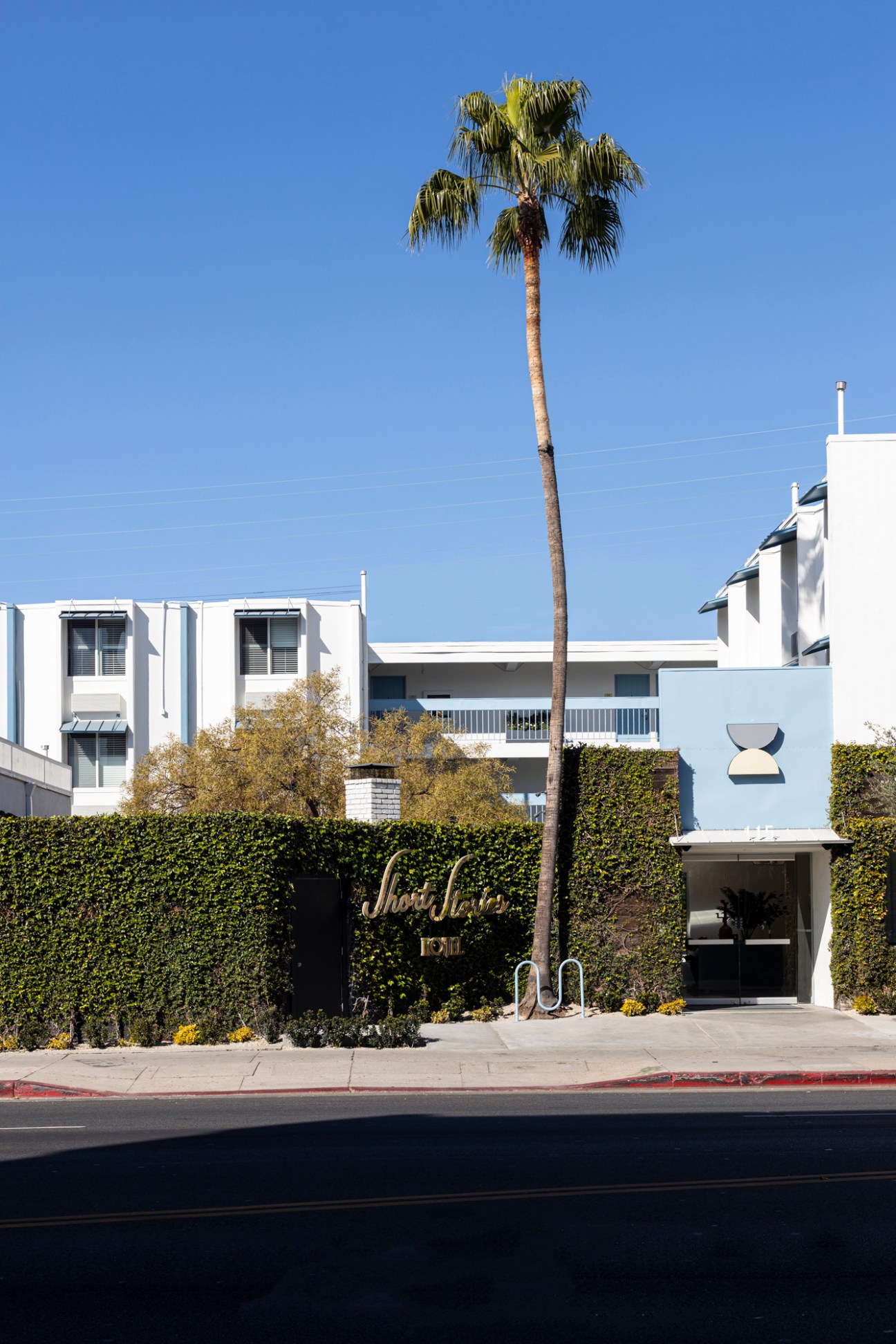 White modernist hotel building with palm tree and ivy-covered entrance wall featuring Short Stories signage