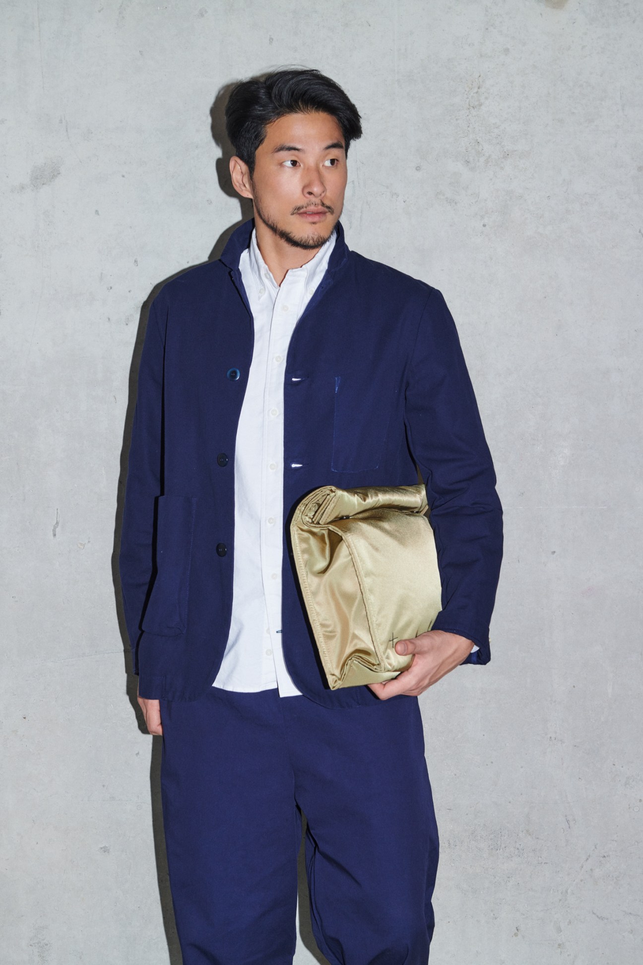 Man in coordinated navy jacket and trousers with white shirt holding golden bag