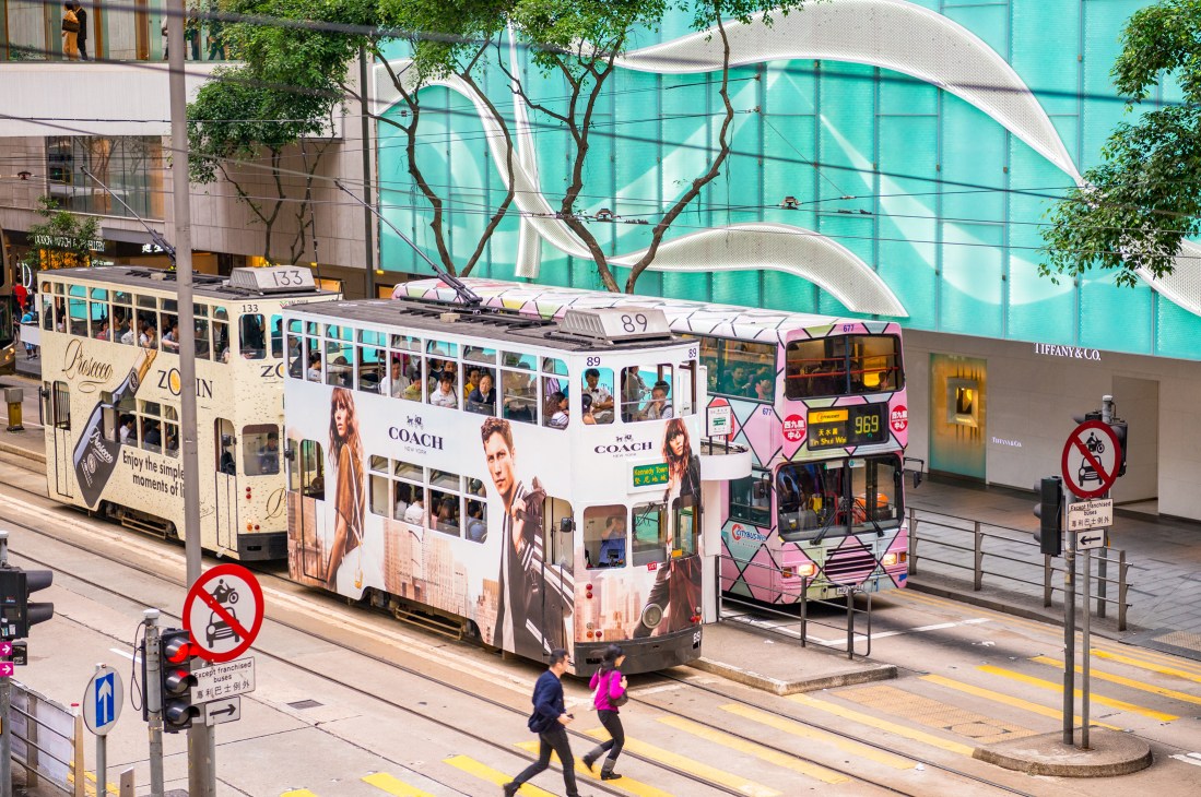 Hong Kong double-decker trams with Coach brand advertisements on their sides at a city street stop