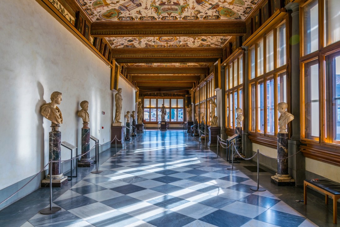 Classical corridor with marble busts on pedestals, ornate gold ceiling, and diamond-patterned floor.