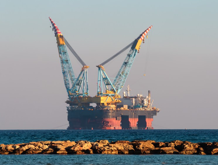 A large offshore oil platform with towering cranes sits on calm open water at dusk.